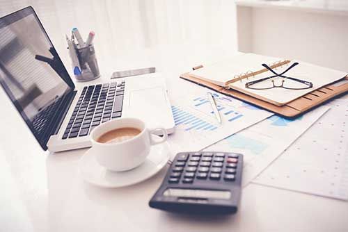 A Desk with A Laptop, Calculator, Cup Of Coffee And Glasses — Blue Chip Bookkeeping In Cranbrook, QLD