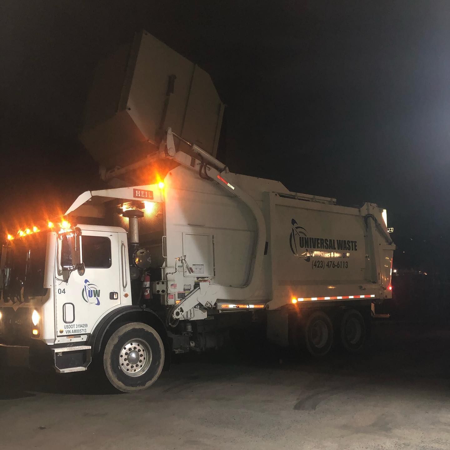 A garbage truck is parked in a parking lot at night