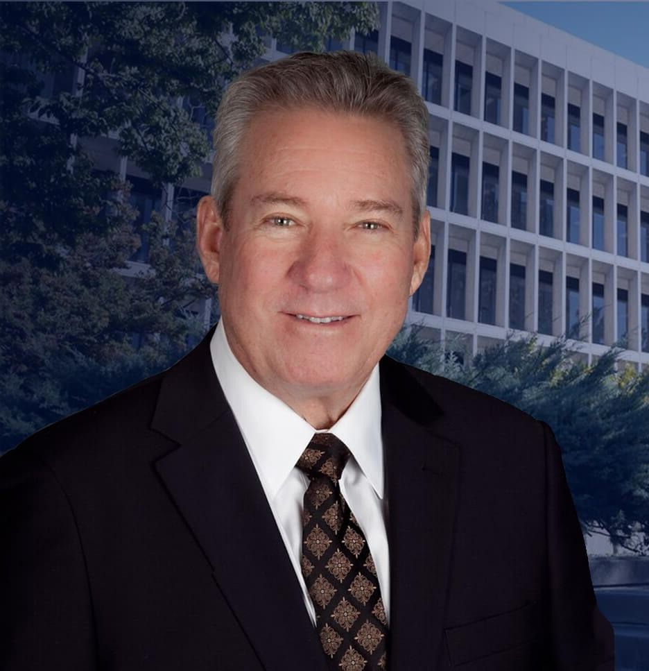 Portrait of a smiling man in a suit and tie, posed before a modern office building background