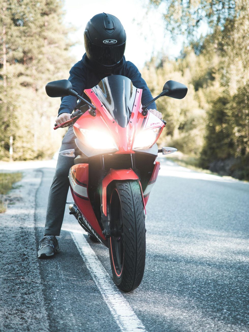 Motorcyclist on a red sport bike on a sunlit road, viewed from the front with headlights on