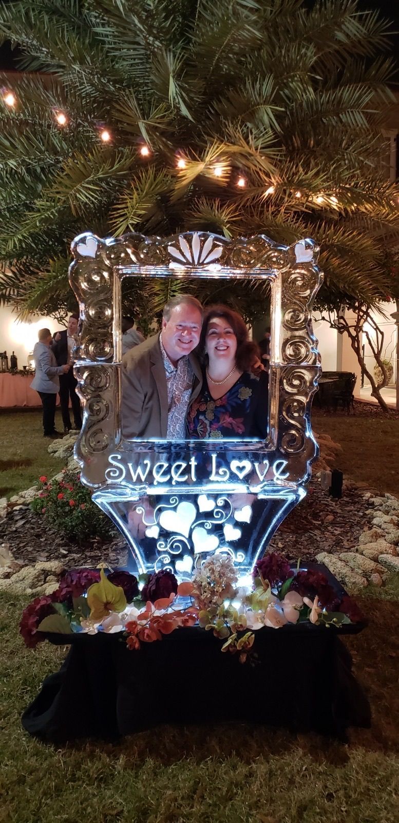A Man and Woman Pose in front of a Sweet Love Ice Sculpture