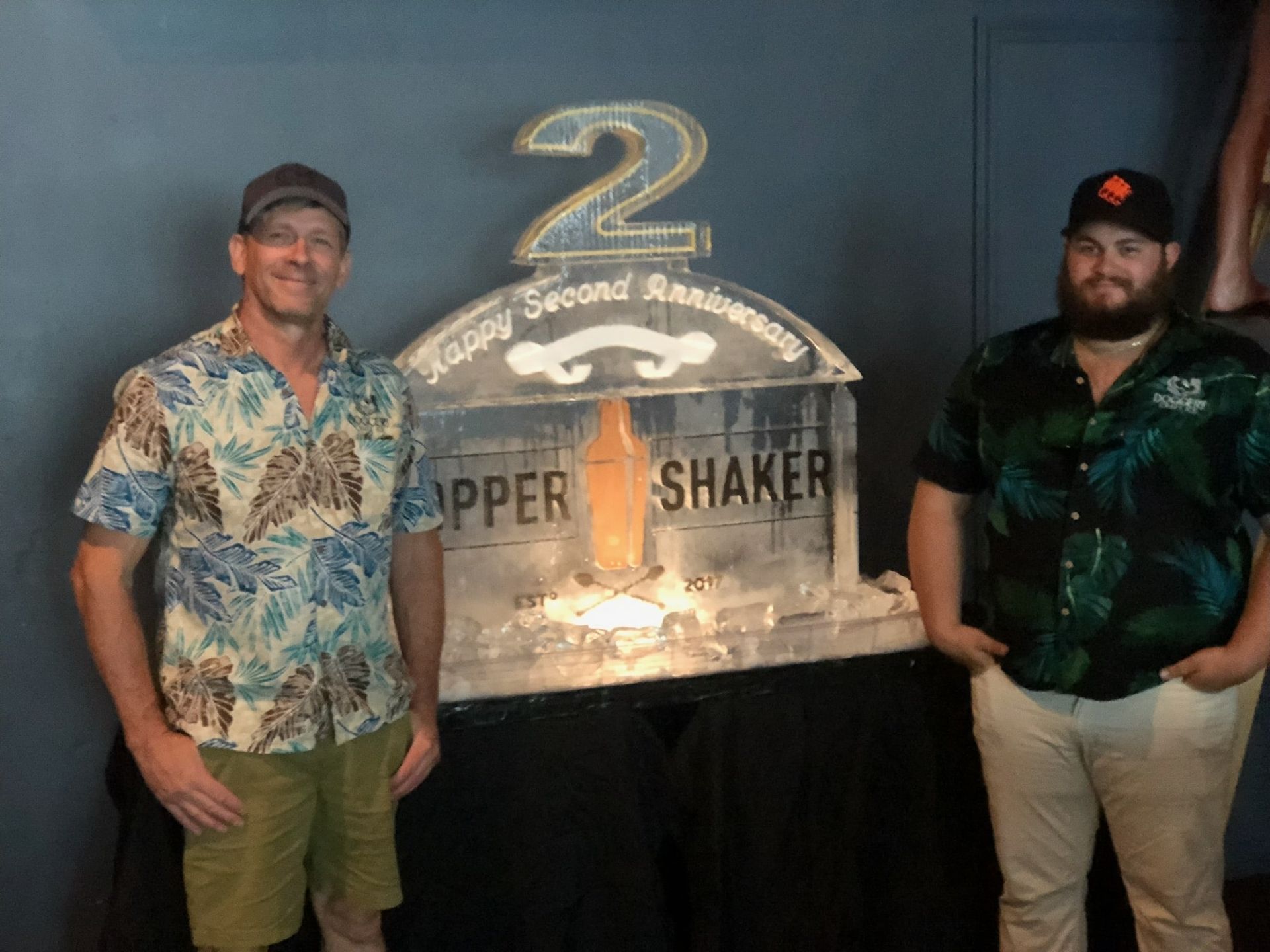 Two Men Standing in front of an Ice Sculpture that says Happy Second Anniversary