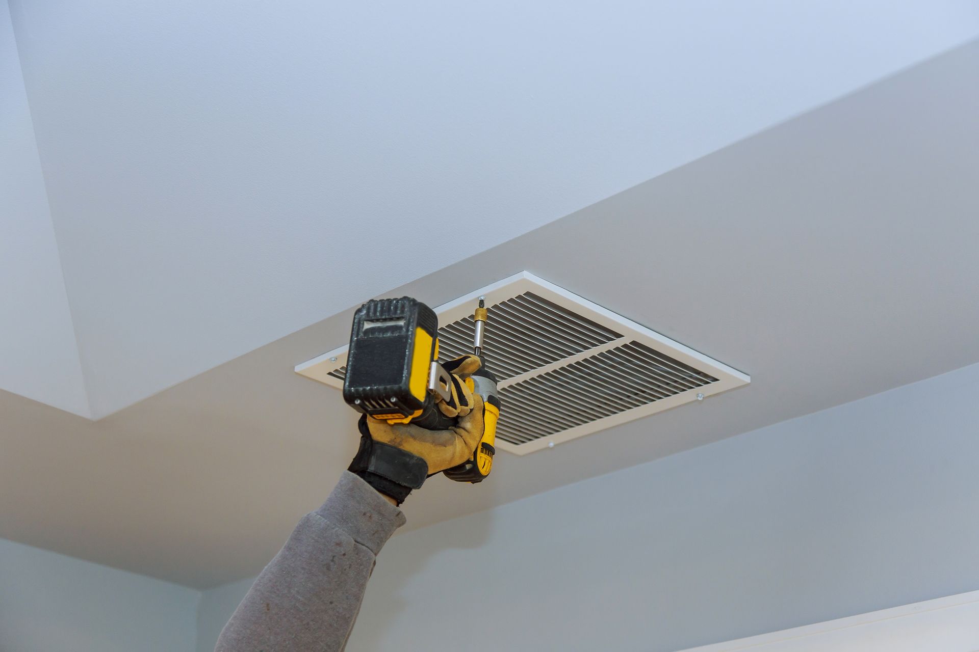 a person is using a drill to install an air vent in the ceiling .