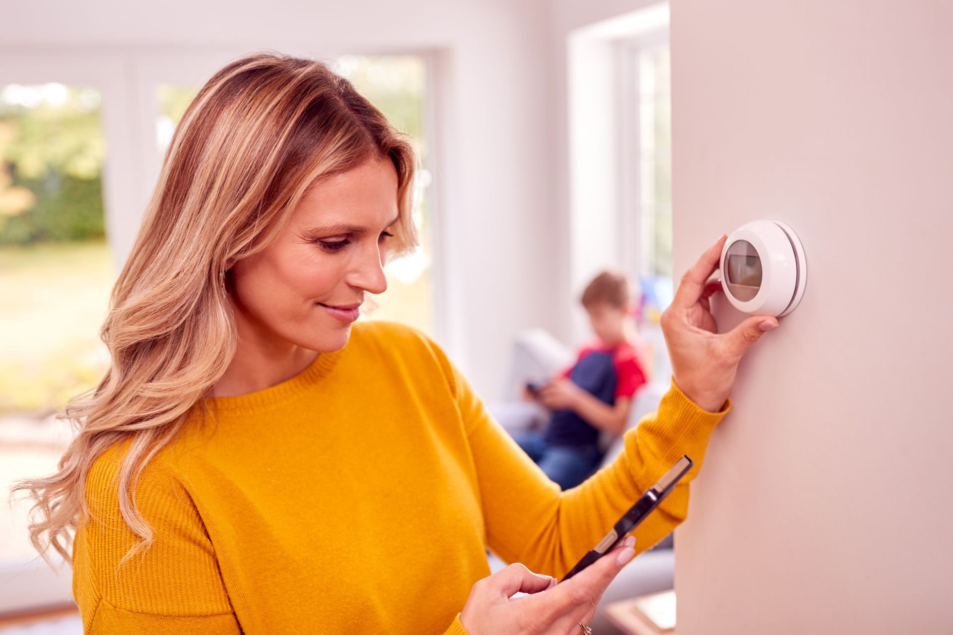 a woman is adjusting a thermostat on a wall while using a smart phone .