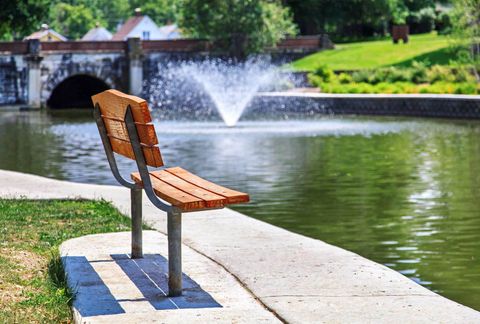 Park bench overlooking a lagoon, with fountain and bridge in the background. This scene is located at Miller Park in Bloomington, Illinois