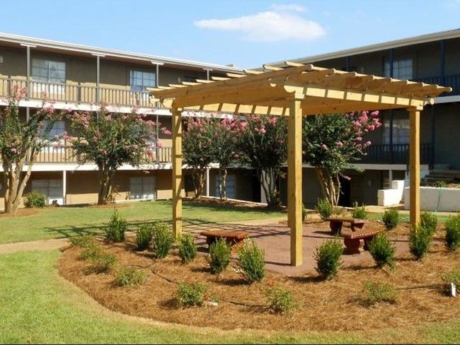 A pergola with a picnic table underneath it in front of a building