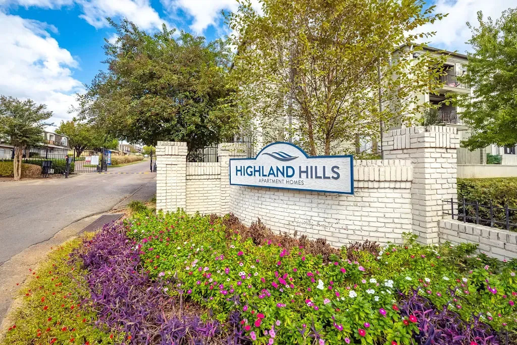 A sign for highland hills is surrounded by flowers and trees.