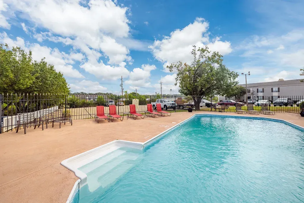 A large swimming pool surrounded by red chairs and a fence.