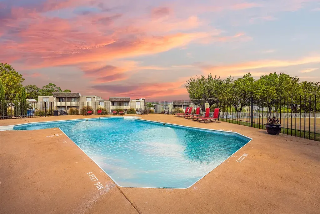 A large swimming pool surrounded by a fence and chairs at sunset.