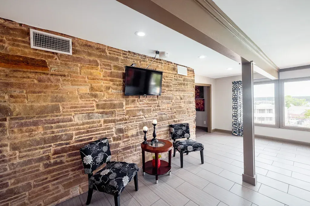 A living room with a brick wall , chairs , a table and a flat screen tv.