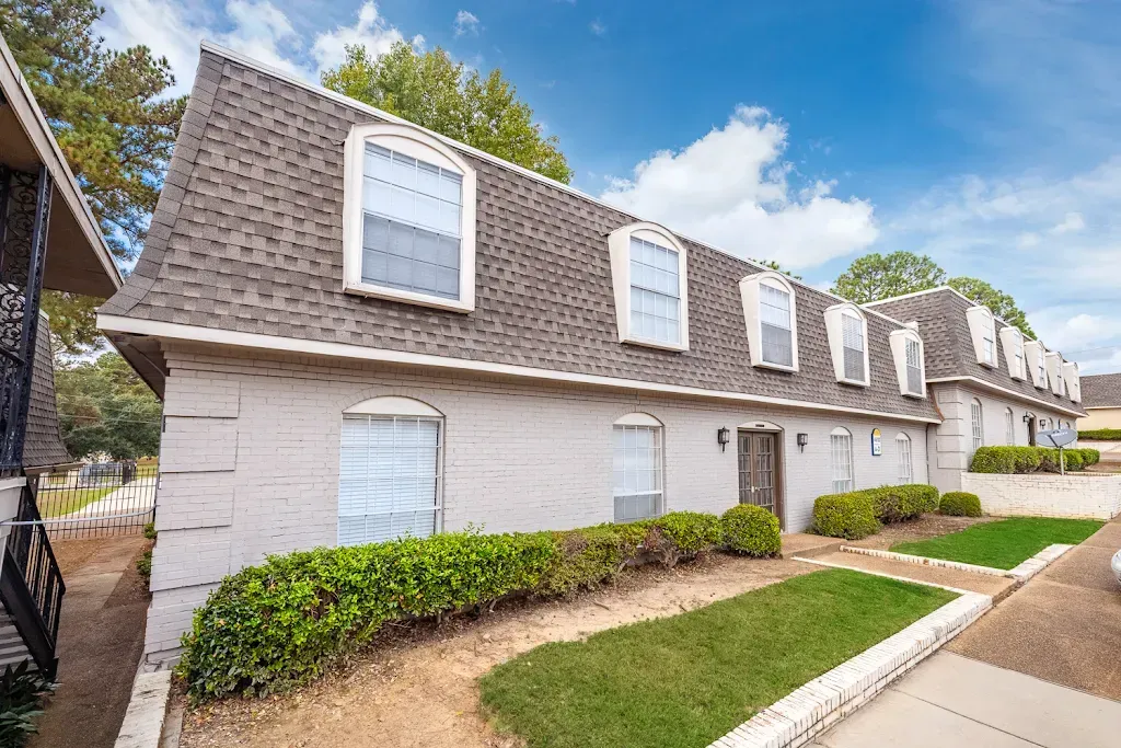 A white brick apartment building with a gray roof and a lot of windows.