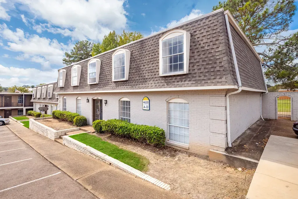 A white apartment building with a lot of windows and a parking lot in front of it.
