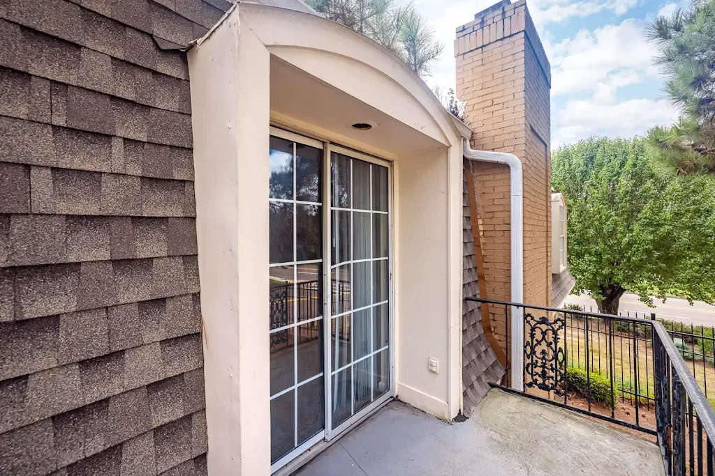 A balcony with a sliding glass door and a brick building in the background.