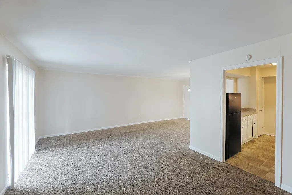 An empty living room with a sliding glass door and a refrigerator.