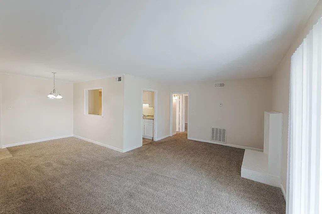An empty living room with a carpeted floor and white walls.