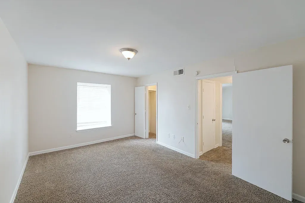 An empty bedroom with a carpeted floor and a window.