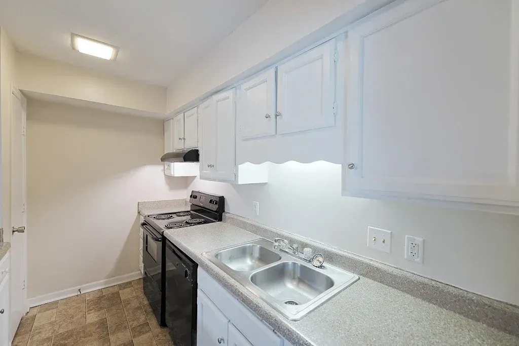 A kitchen with white cabinets , a sink , stove and dishwasher.