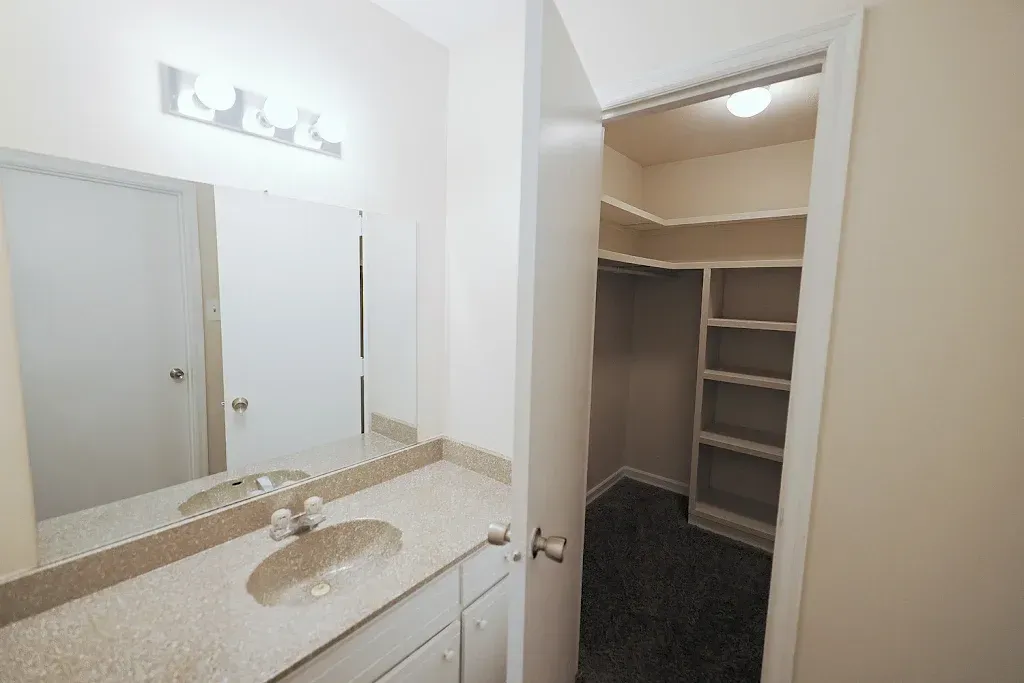 A bathroom with a sink , mirror and walk in closet.