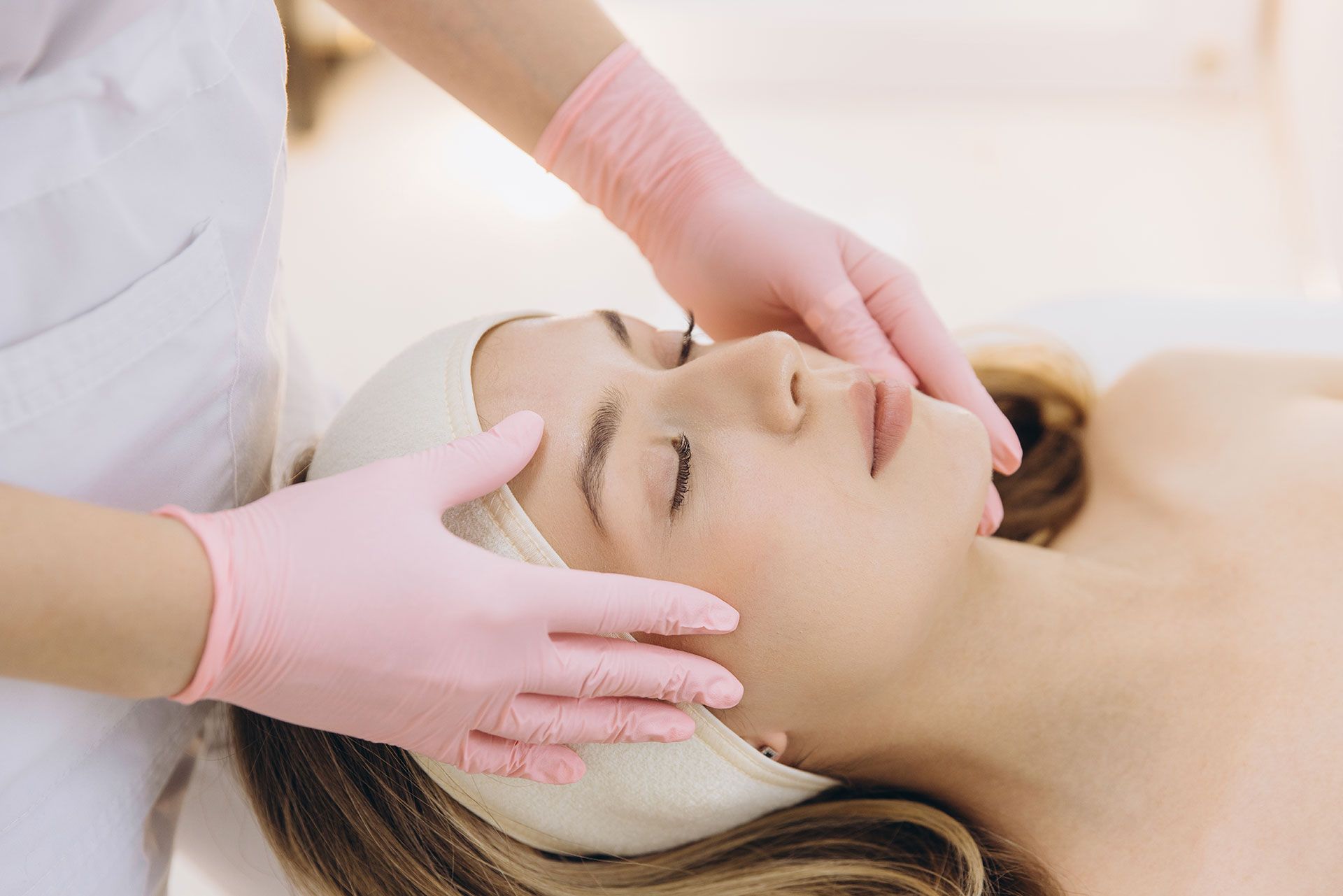 Woman receiving facial massage; pink gloves, spa setting.