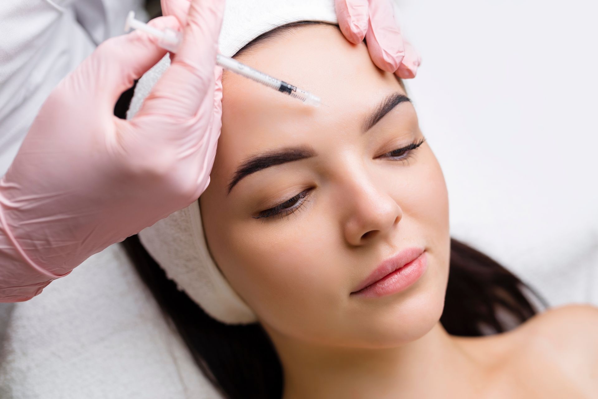 Person receiving a Botox injection in their forehead. A healthcare professional with pink gloves holds a syringe.