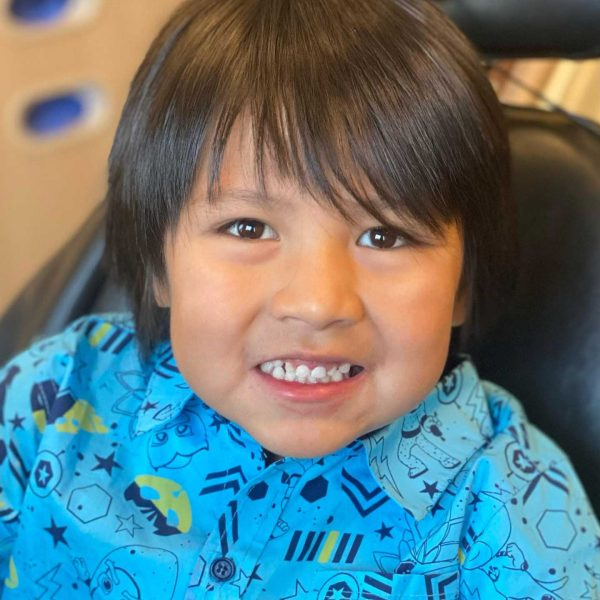 Boy with brown hair and a blue patterned shirt smiling, close-up.
