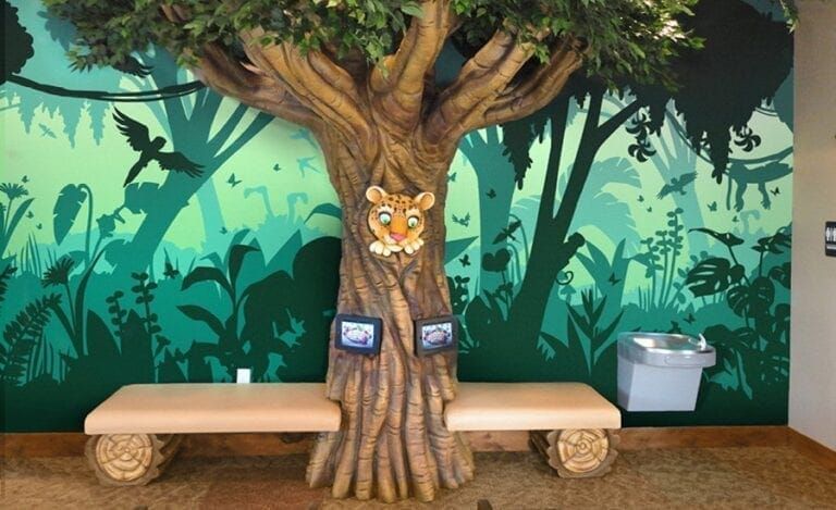 Tree with benches and mural backdrop in a play area.  Water fountain and tiger face on the tree.