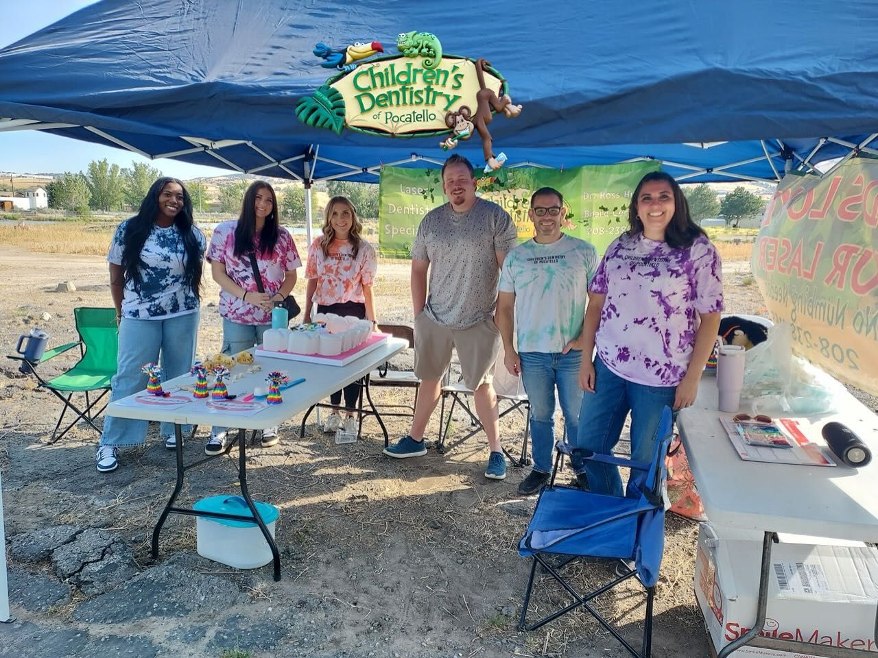 Children's dentistry booth outdoors with staff in tie-dye shirts, under a tent. 