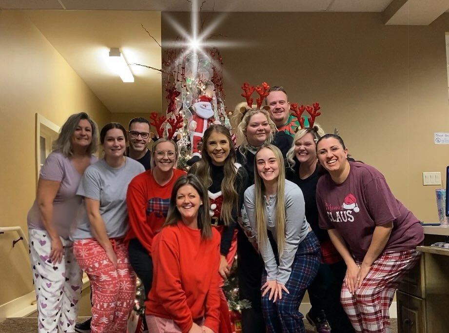 Group of people in pajamas pose in front of a decorated Christmas tree.
