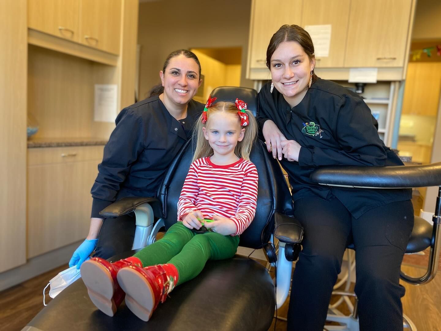 Smiling child in dental chair with two dental assistants.