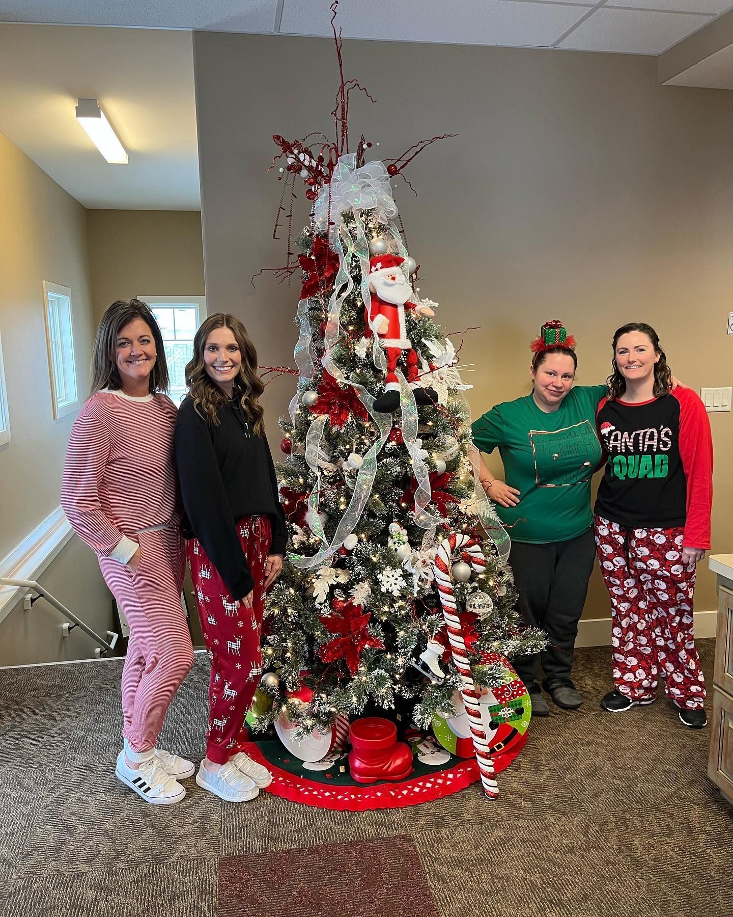 Four people pose by a decorated Christmas tree, wearing festive pajamas.