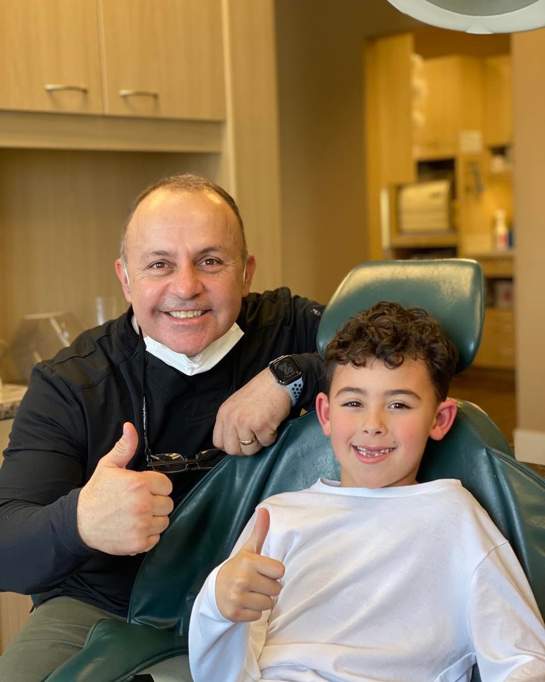 Man and child in dental chair give thumbs up. Dental office setting.