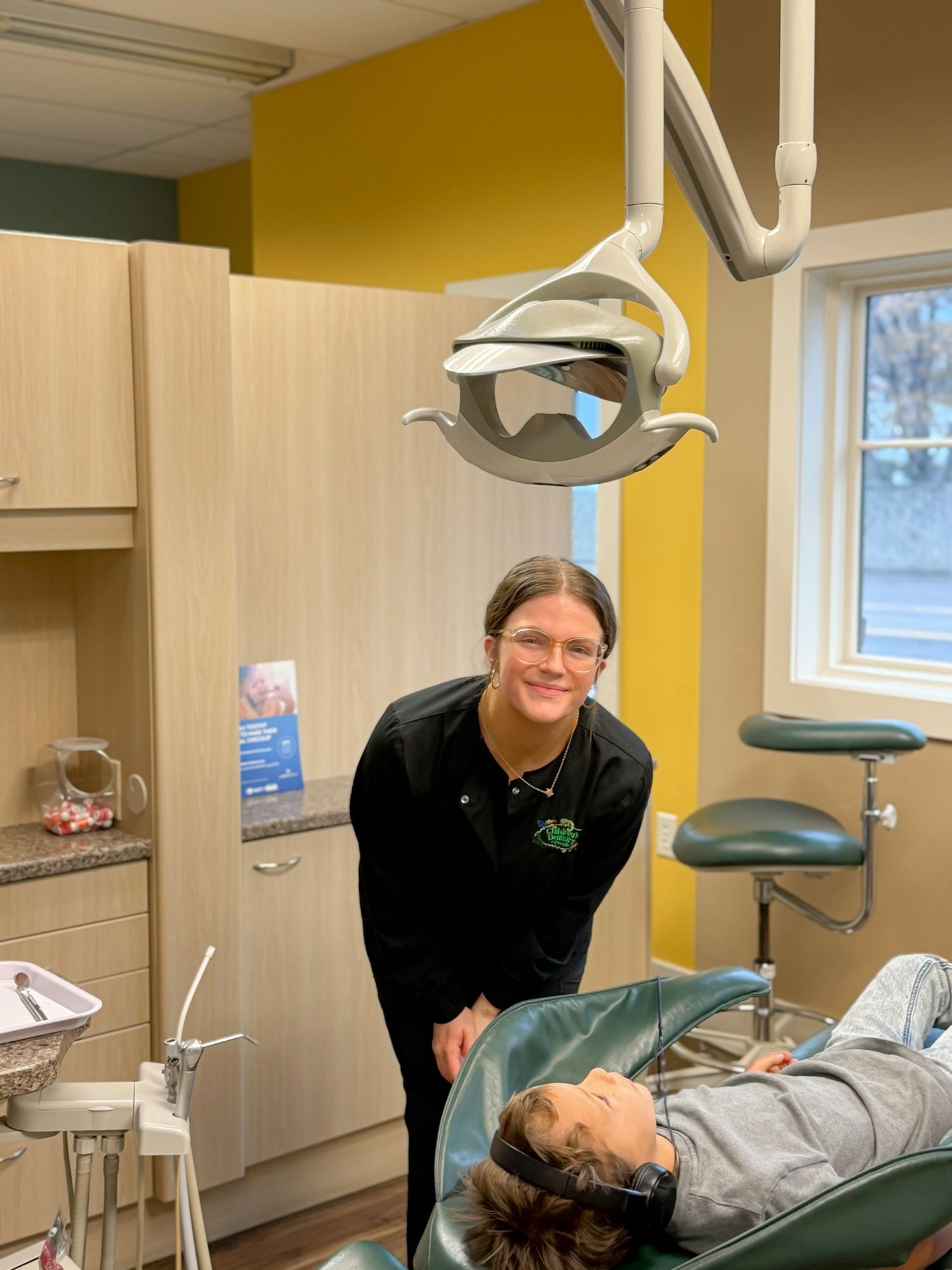 Dental assistant with patient in dental chair, modern office setting.