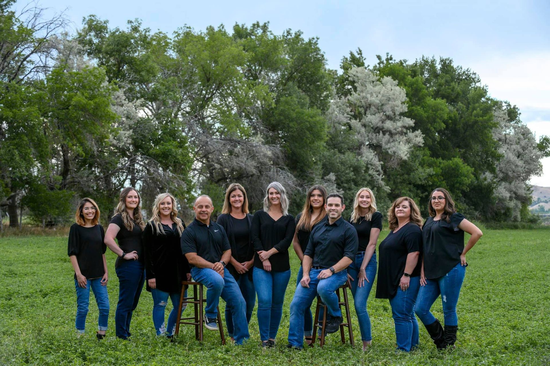 Group of people in black shirts and jeans pose outdoors.