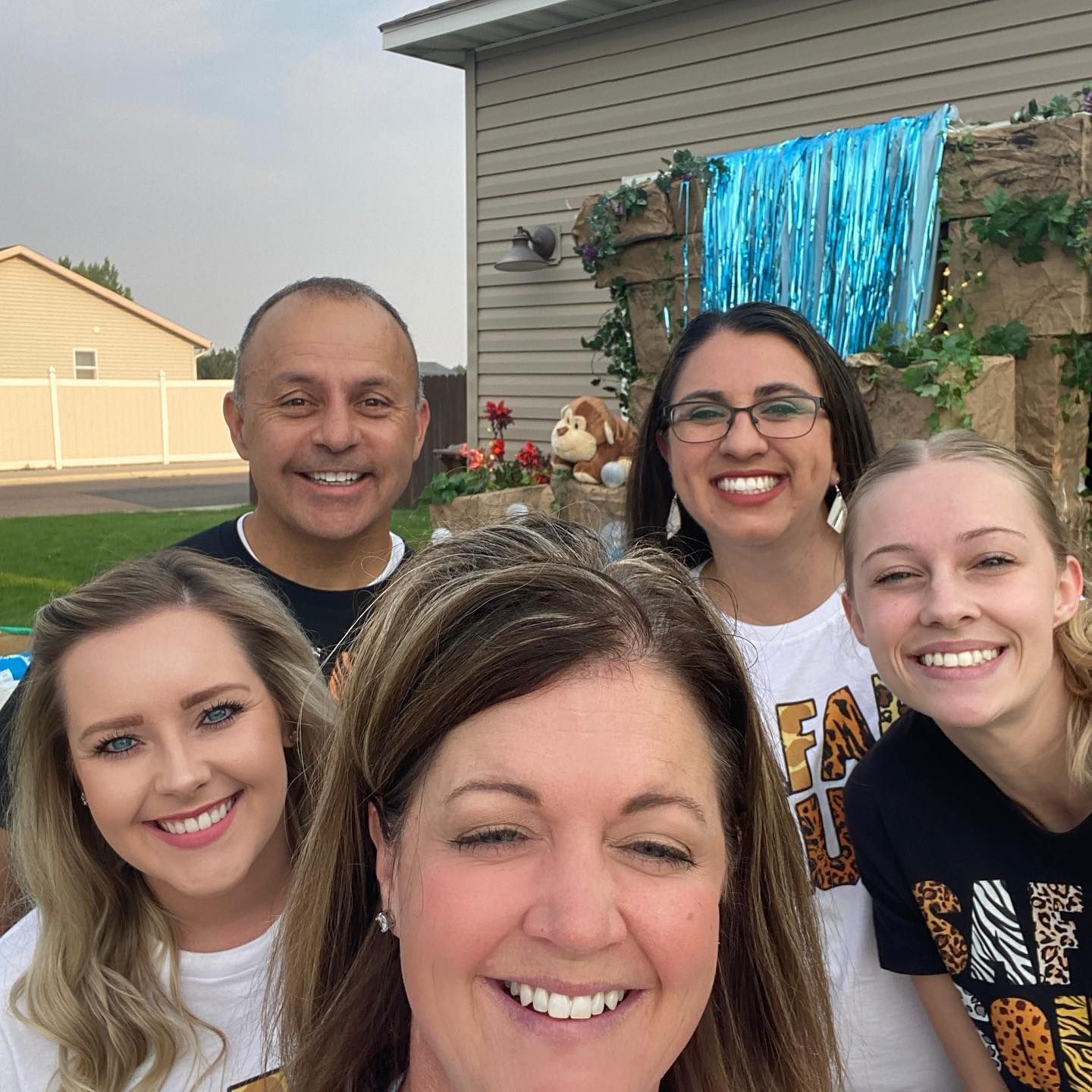 Group of five people smiling outdoors in front of decorated structure with blue fringe.