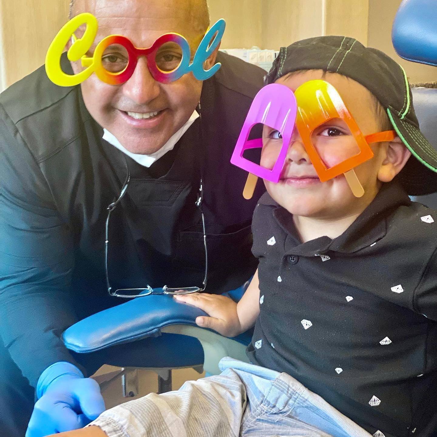 Dentist and child in dental chair wearing novelty glasses, smiling.
