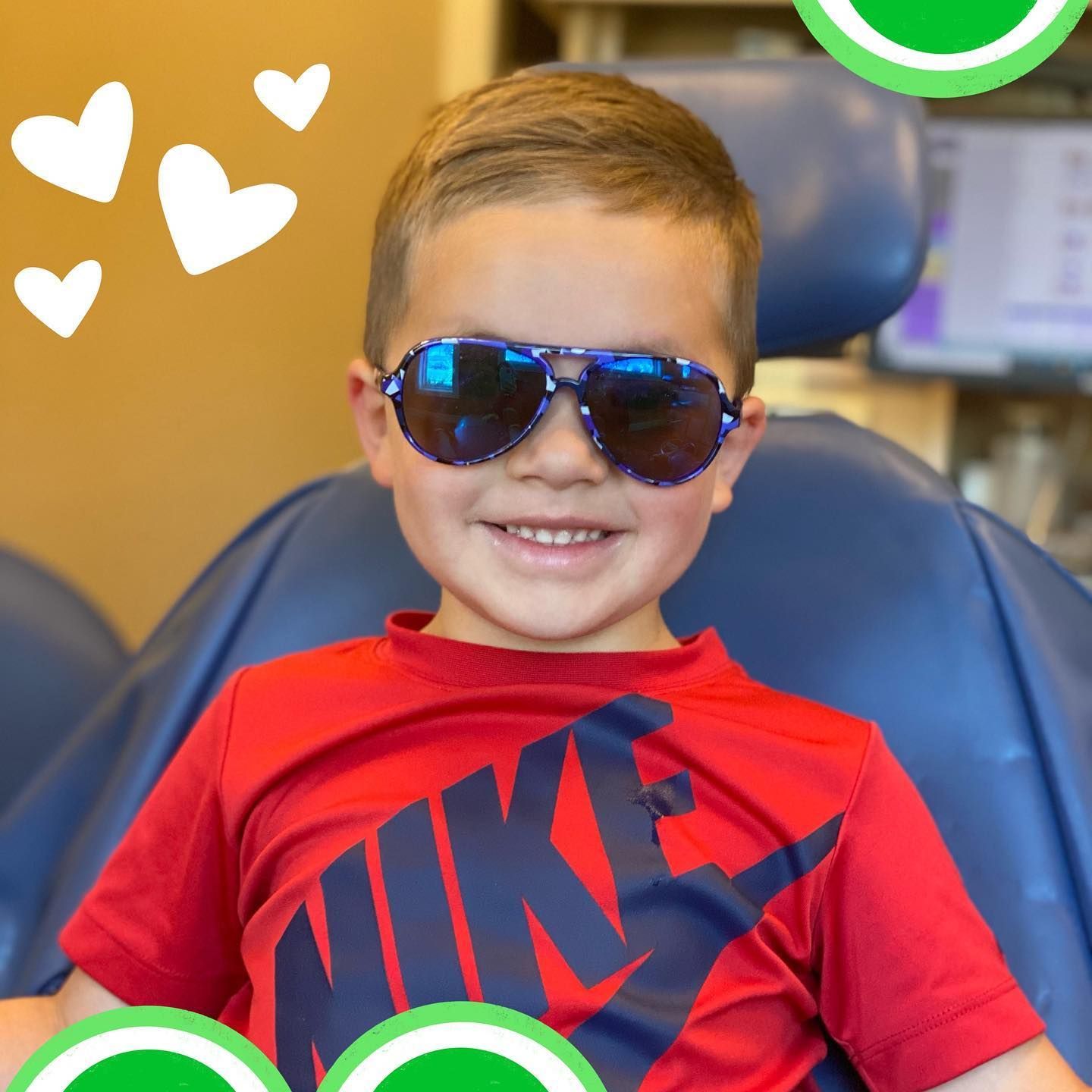 Boy with sunglasses and a red Nike shirt smiles in a blue dentist chair.