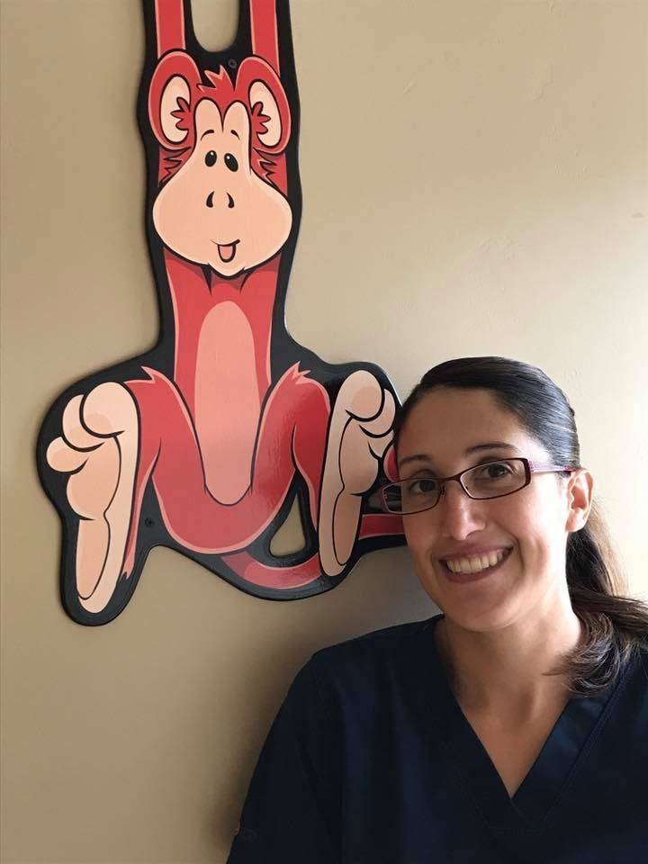 Woman in blue scrubs smiles next to a cartoon monkey decoration.