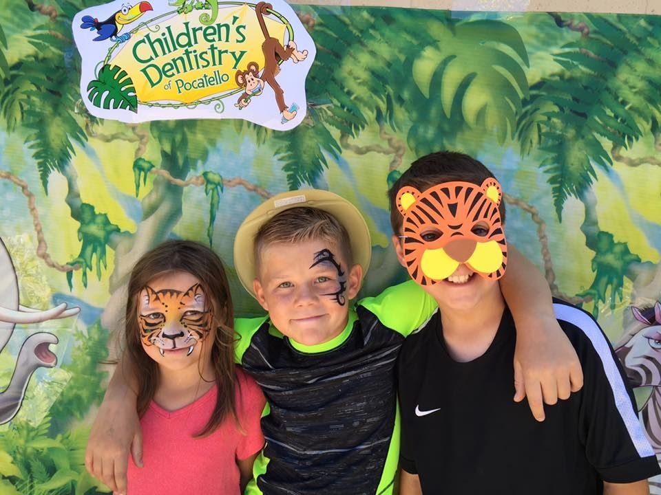 Three children with tiger face paint pose in front of a jungle-themed backdrop.