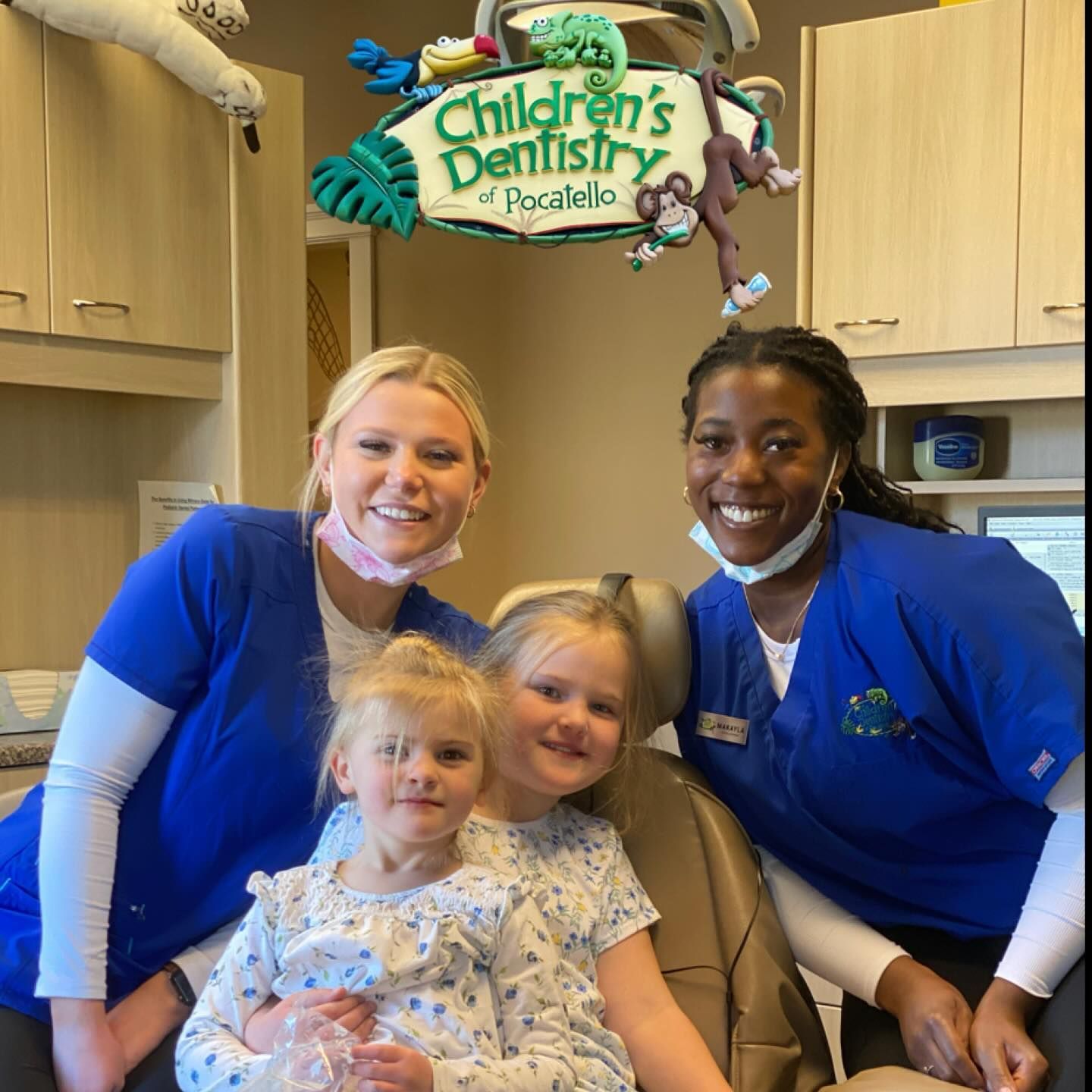 Two dental staff with two young children at a dentist's office. Smiling. Sign says 
