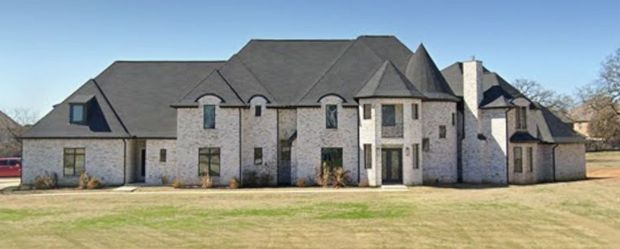 A large white house with a gray roof is sitting in the middle of a grassy field.