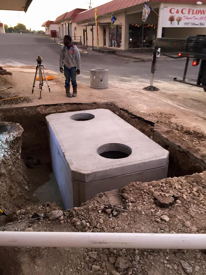 A man is standing in a hole next to a septic tank.