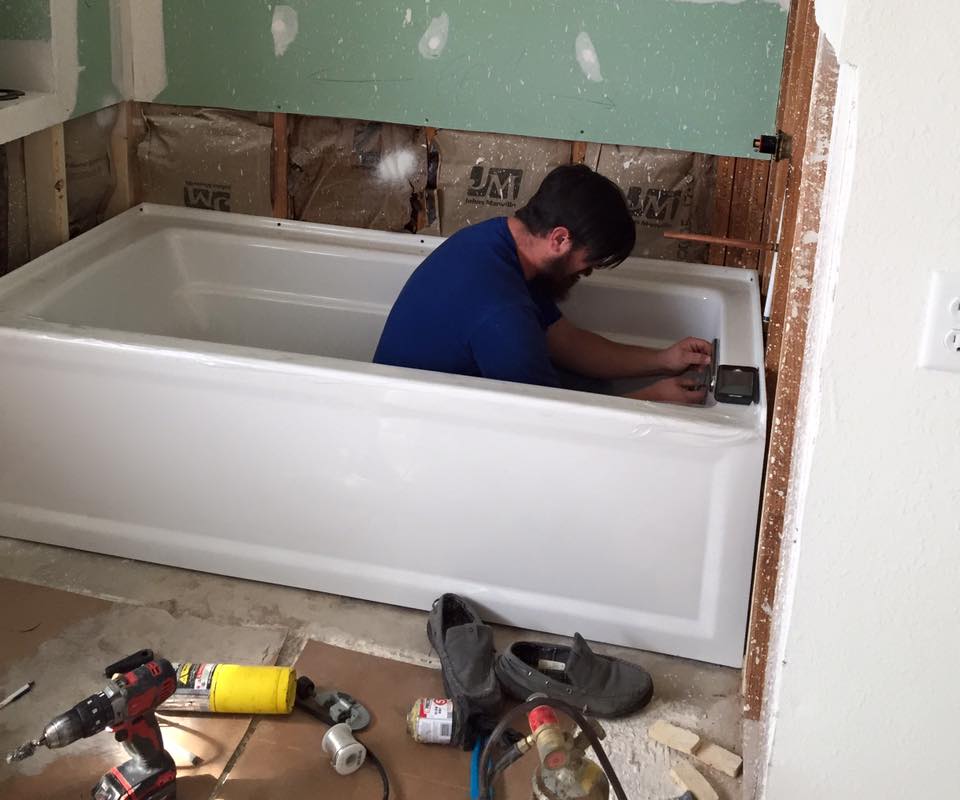 A man is working on a bathtub in a bathroom.