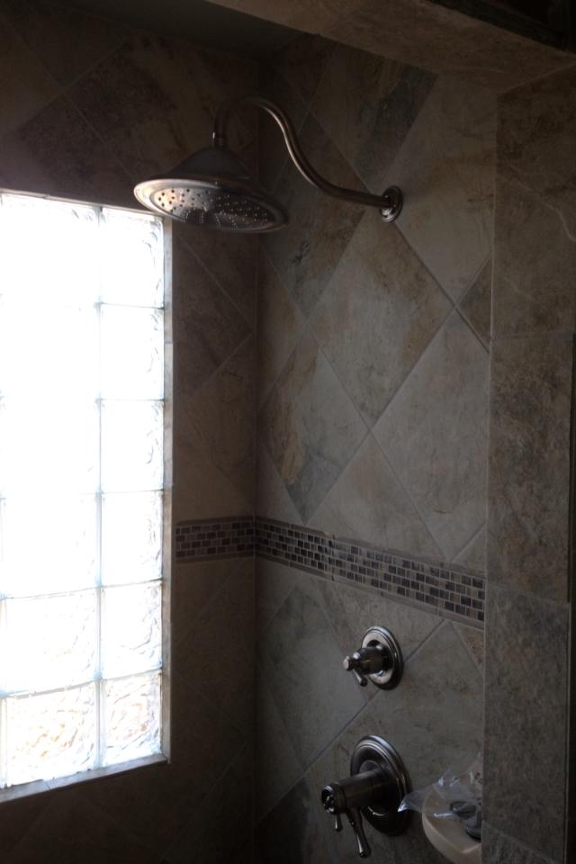 A shower head is hanging from the ceiling in a bathroom next to a window.