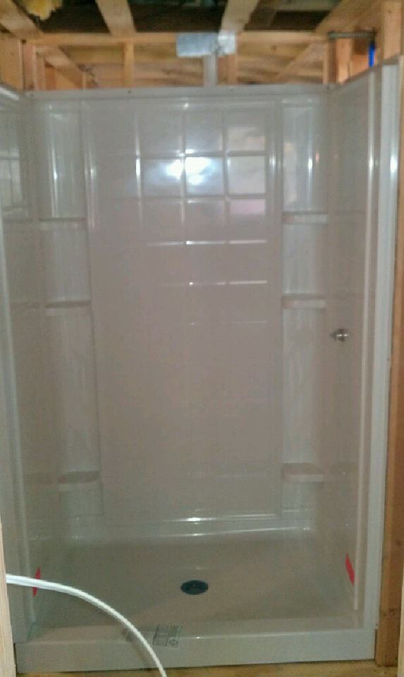 A white shower stall in a bathroom under construction.
