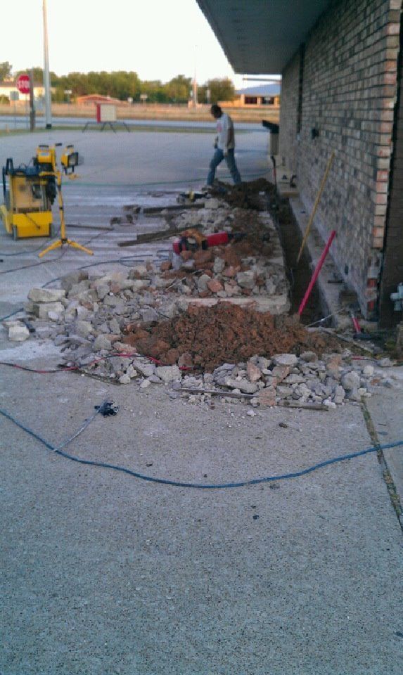 A pile of rocks and dirt is sitting on the sidewalk in front of a brick building.