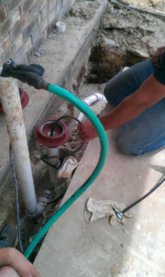 A person is kneeling down next to a green hose.