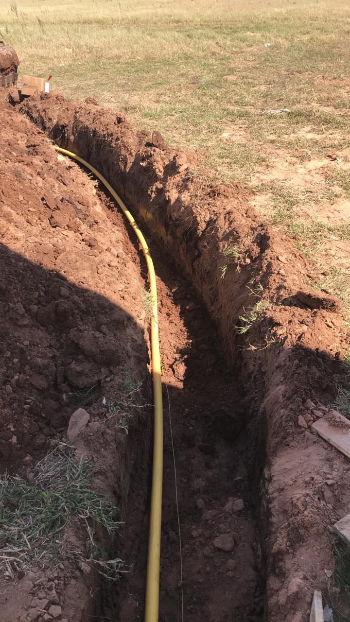 A yellow pipe is being installed in a trench in the dirt.