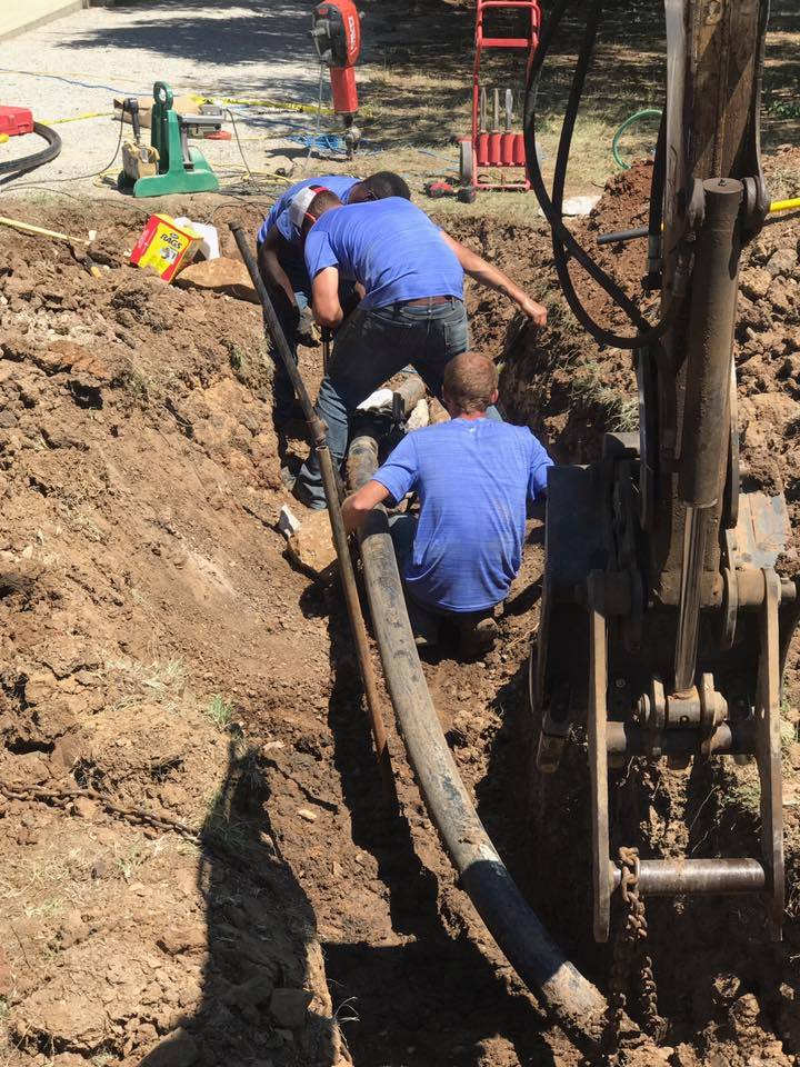 A group of men in blue shirts are working in the dirt.