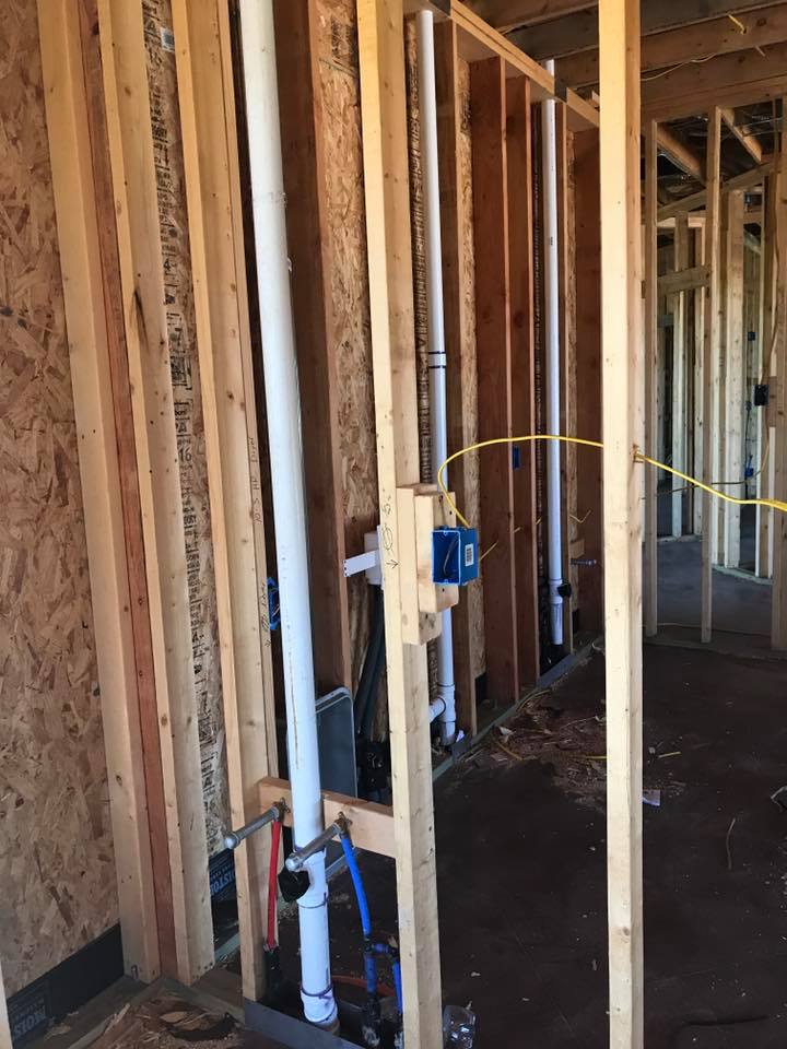 A room in a house under construction with pipes coming out of the wall.