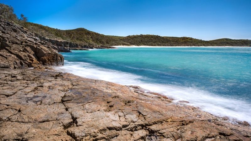 A Rocky Beach With A Large Body Of Water In The Background —Homemakers Lifestyle In Noosa, QLD